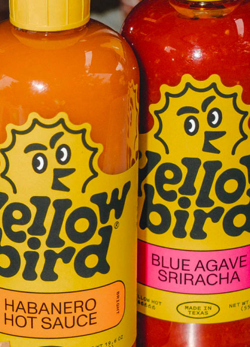 A picture of a 19.6 ounce Yellowbird habanero hot sauce bottle next to a 19.6 ounce Yellowbird blue agave sriracha hot sauce bottle