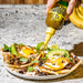 Yellowbird Classic Serrano Hot Sauce drizzled onto egg, sausage, potato, and cheese breakfast tacos
