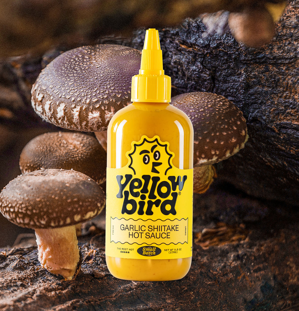 Yellowbird Small Batch Garlic Shiitake Hot Sauce 9.8 oz. with shiitake mushrooms in background